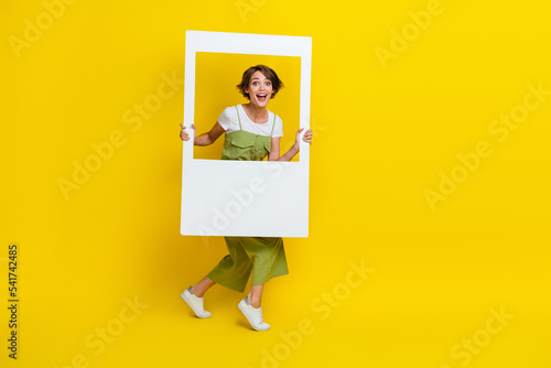 Full body size photo of pretty cute girl wear khaki outfit hold paper white window excited take photo shot repost isolated on yellow color background