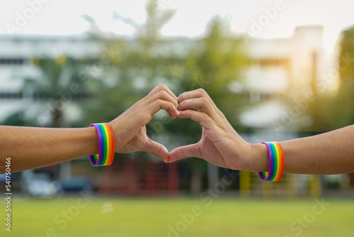 A young Asian Lgbt couple wearing rainbow wristbands put their hands together in a heart shape. to show love Pride of being LGBT. soft and selective focus.