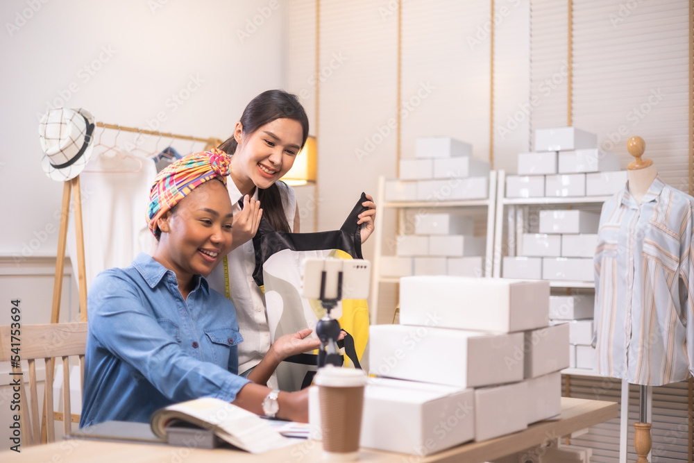 Two asian and african american woman business owner fashion designer cloth tailor creative working for new collection.Happy online store owner preparing an order for shipping . Two asian and african american woman business owner fashion designer cloth tailor creative working for new collection.Happy online store owner preparing an order for shipping .