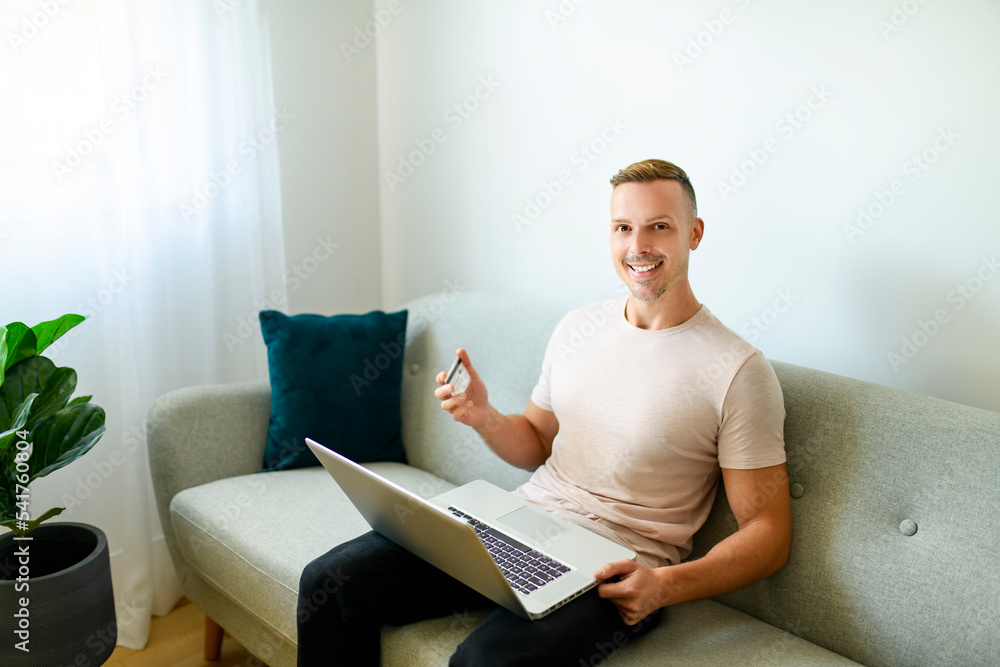 technology, people and online shopping concept - happy smiling man with laptop computer and credit card at home