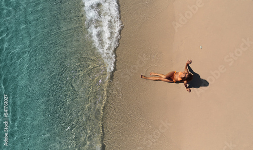 Aerial view of a beautiful woman wearing an orange bikini while sunbathing along the sandy shoreline in front a crystalline sea in San Sostene, Calabria, Italy. photo