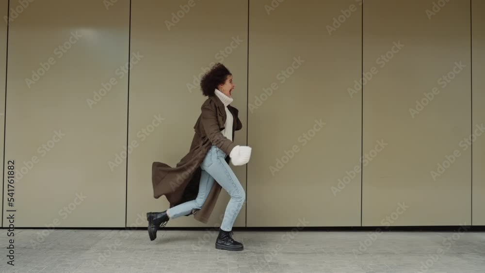 custom made wallpaper toronto digitalSide view following happy cheerful curly hair girl runs jump turning around smiling happily near modern building wall in city street, urban style joyful young woman in trendy autumn coat walking alone