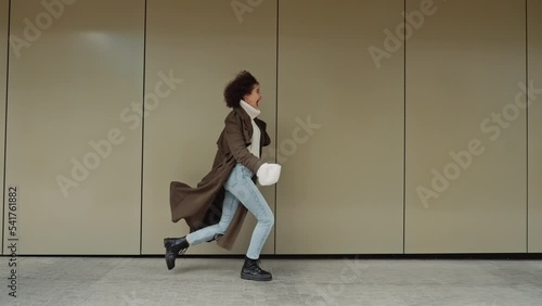 Wallpaper Mural Side view following happy cheerful curly hair girl runs jump turning around smiling happily near modern building wall in city street, urban style joyful young woman in trendy autumn coat walking alone Torontodigital.ca