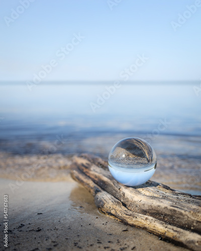 Butterfly on a glass ball on the beach reflecting the lake and sky. Concept of tranquility and zen.  © Alaskajade
