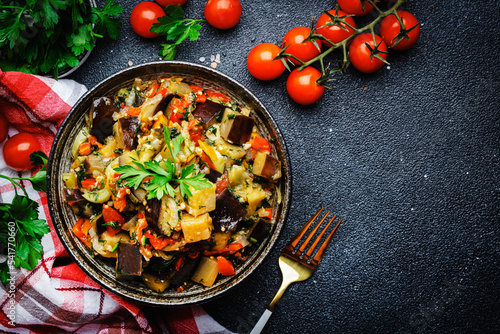 Vegetable stew, saute or caponata. Stewed eggplant with paprika, tomatoes, herbs and spices. Black kitchen table background, top view, copy space
