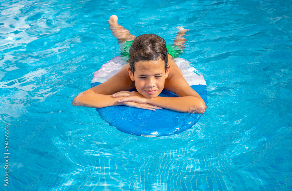 Cute smiling child boy paddling on the surf board in pool