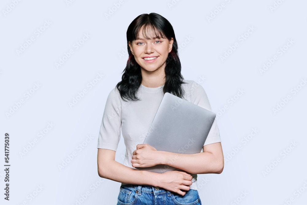 Teenage female student with laptop, looking at camera on light background Teenage female student with laptop, looking at camera on light background