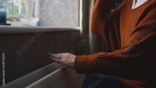 Close up of senior woman sitting by radiator at home trying to keep warm during energy and cost of living crisis drinking hot drink and shivering - shot in slow motion  photo