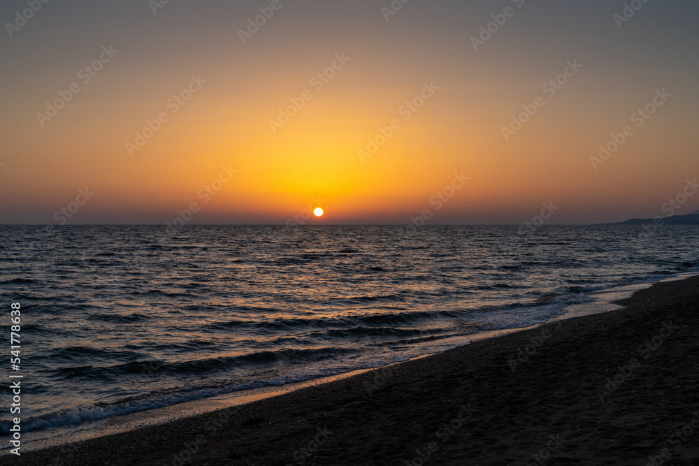 sunset on the Mediterranean Sea in Greece with calm ocean water and dark sand beach in the foreground sunset on the Mediterranean Sea in Greece with calm ocean water and dark sand beach in the foreground