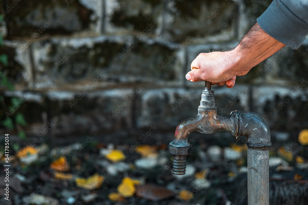Close-up of a street tap for water against the background of yellow leaves. Hand opening a water faucet.