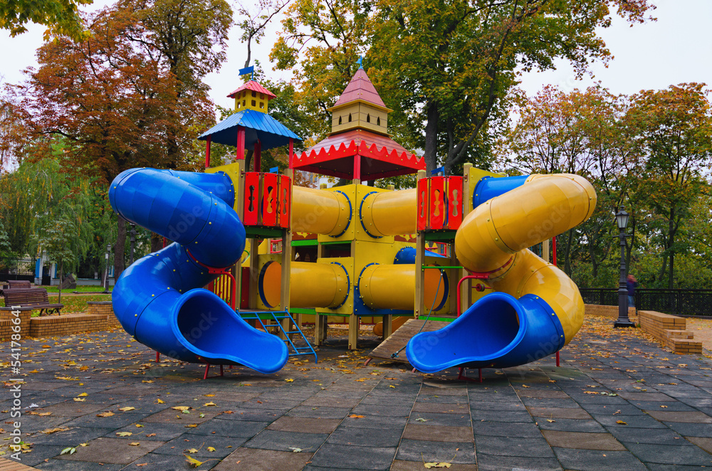 Colorful modern playground for little kids in the city park. An empty children's playground is waiting for children. Early morning in Saint Volodymyr Hill. Autumn colored trees in the background