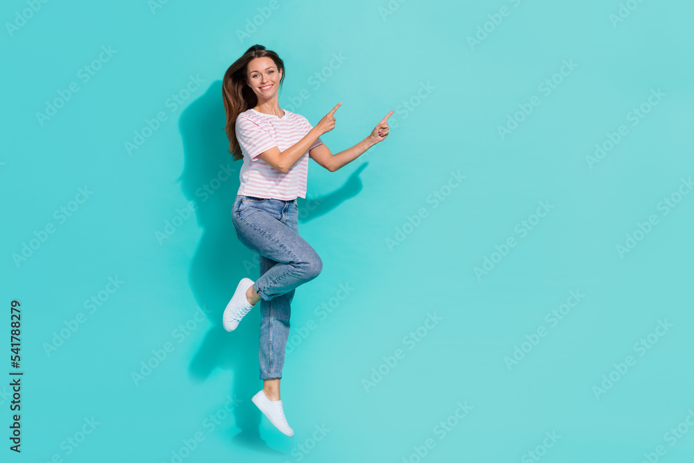 Full size photo of flying nice woman with straight hairdo wear striped t-shirt directing empty space isolated on teal color background Full size photo of flying nice woman with straight hairdo wear striped t-shirt directing empty space isolated on teal color background