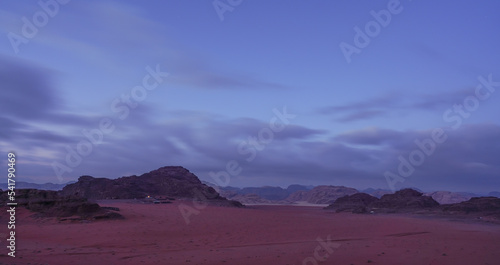 Rocky scenery in Wadi Rum desert during early overcast morning  camp light at distance visible