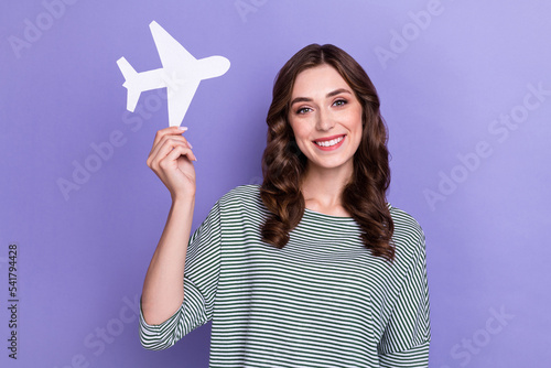 Photo of positive cheerful glamour lady hand hold paper card plane advertise travel agency service isolated on purple color background
