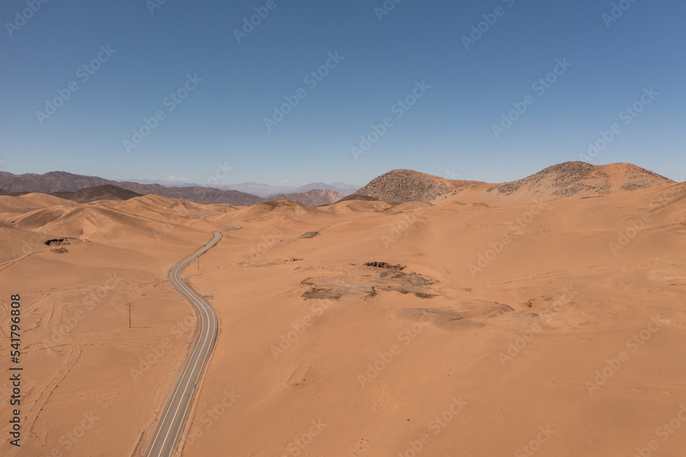 Aerial photo of a road in the atacama desert with a blue sky and mountains behind Aerial photo of a road in the atacama desert with a blue sky and mountains behind