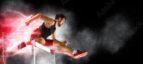 Man athlete at hurdle race, jumping over the last hurdle photo