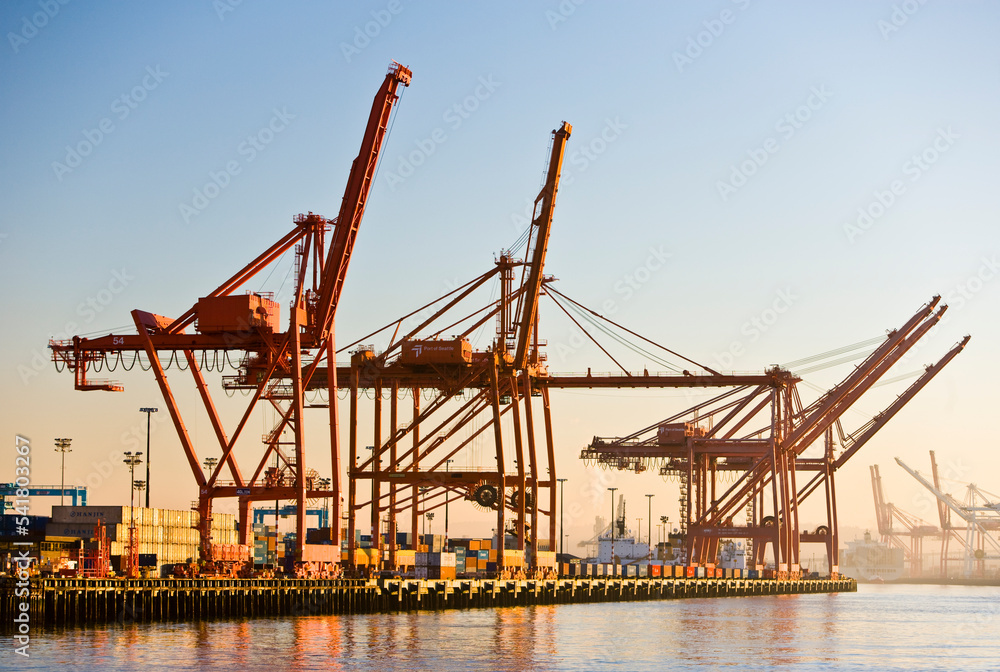 Cargo container cranes at a port wait for a ship to load at sunset 
