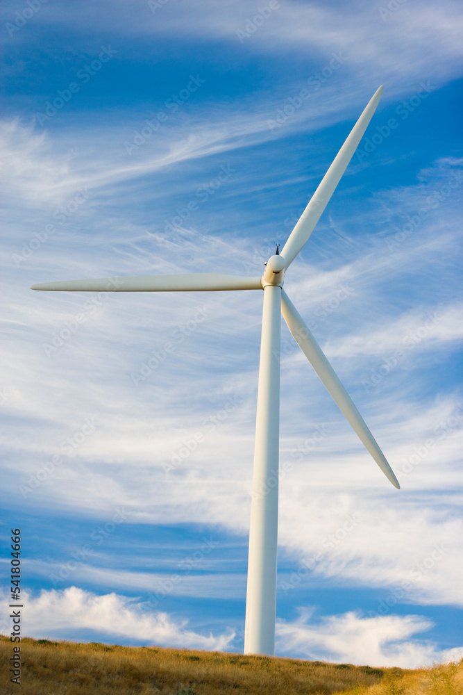 A single windmill sits quietly against a crisp, blue sky with wispy white clouds on a hill A single windmill sits quietly against a crisp, blue sky with wispy white clouds on a hill