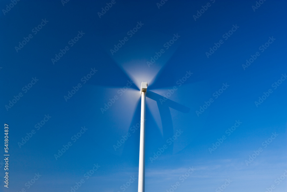 Spinning wind turbine blades with shadow of the nacelle against a clear blue sky.