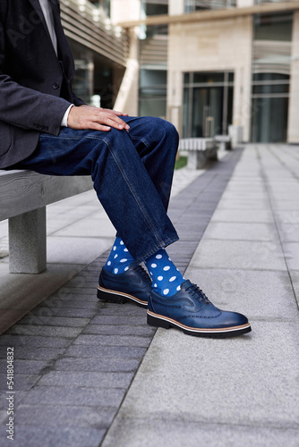 Stylish businessman sits outdoors in blue socks and jeans