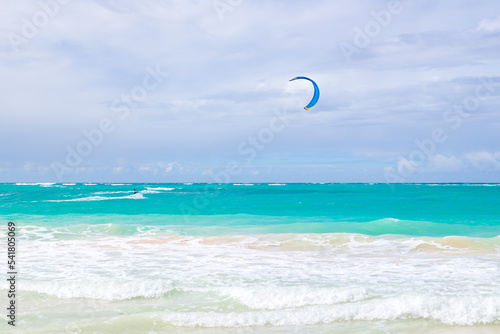 Kite surfer goes over shore waves under blue cloudy sky