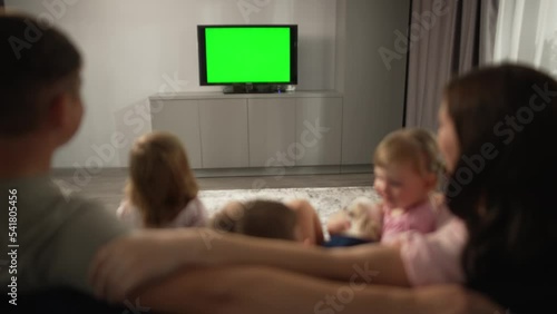 Leisure in the apartment, family in front of the TV on the sofa, children. Three children and a father and mother are relaxing at home, watching a movie, football or a TV program. 4k