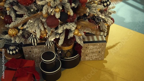 Luxury gift boxes and the Christmas tree decorated with snow, shining lights, golden feathers, carnival-style Christmas tree toys. Buying presents for family in store, holiday shopping in trade center