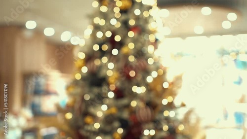 Christmas tree decorated with artificial snow, shining lights, golden feathers, carnival-style Christmas tree toys. Buying gifts for family in cozy shop, traditional holiday shopping in trade center.