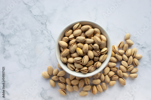 Pistachio nuts in a bowl on white marble background. Close up, top view, copy space. Healthy snack