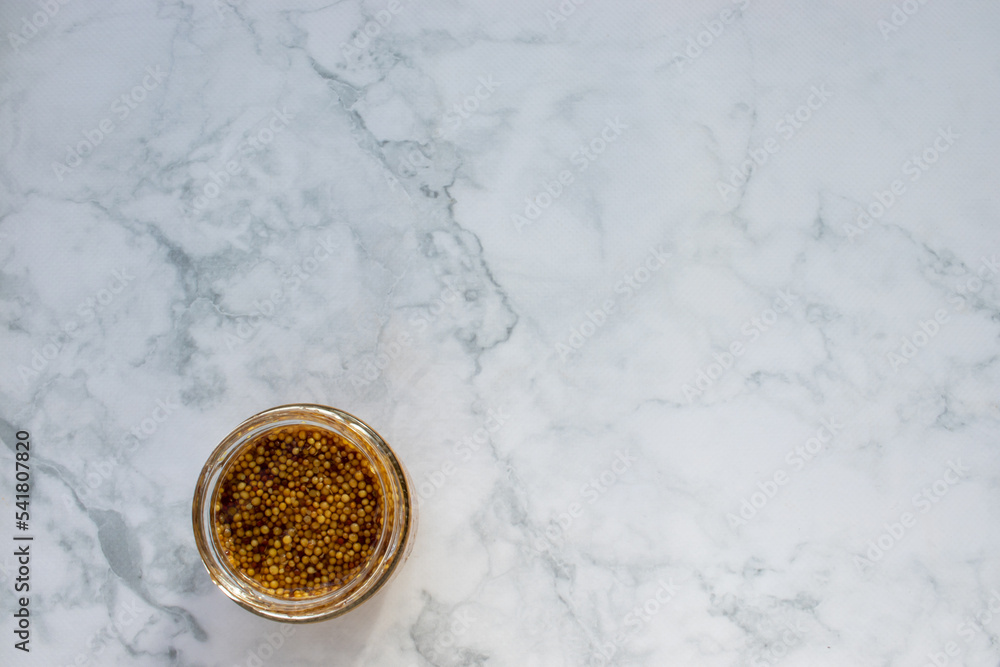 Fototapeta premium Mustard seeds sauce in glass jar on marble table background. Top view, copy space