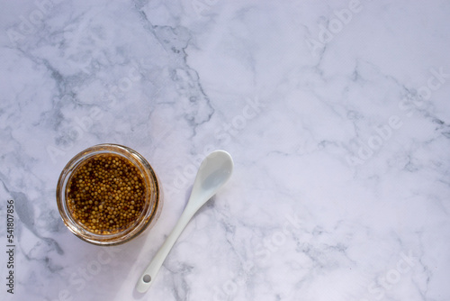 Mustard seeds sauce in glass jar on marble table background. Top view, copy space