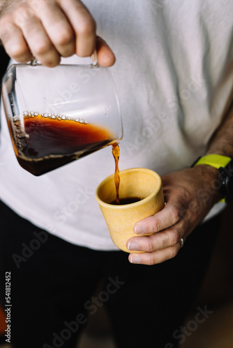 barista pouring a brewed coffee in a yellow cup