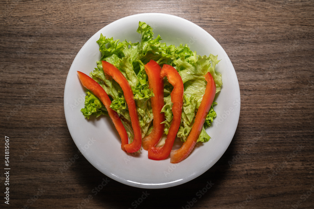 Plate with green lettuce leaves and strips of red pepper on a wooden kitchen worktop Plate with green lettuce leaves and strips of red pepper on a wooden kitchen worktop