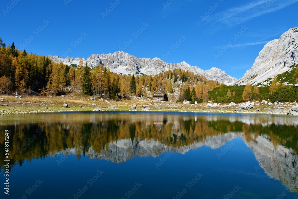 View of the Double lake at Triglav lakes valley with Veliko Spičje mountain behind and a reflection of the mountains and the golden colored larch autumn forest