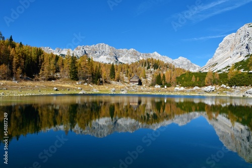 Fototapeta Naklejka Na Ścianę i Meble -  View of the Double lake at Triglav lakes valley with Veliko Spičje mountain behind and a reflection of the mountains and the golden colored larch autumn forest