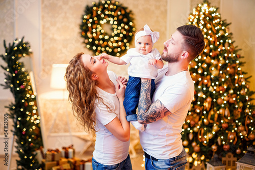 Happy young parents standing near Christmas tree in living room while holding little nice baby girl © zamuruev