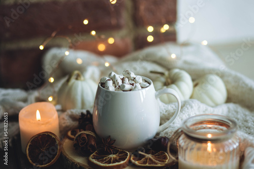 Autumn cozy home composition with hot chocolate with marshmallow and candles. Aromatherapy on a grey fall morning, atmosphere of cosiness and relax. Wooden background, window sill, close up.