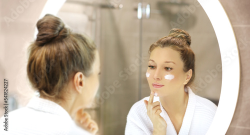 woman looking in the mirror in the bathroom and taking care of her skin.Applying the cream .Magic anti-aging cream.
