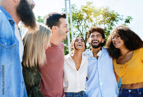 Young group of happy friends having fun laughing together outdoors. Hipster millennial teenage people enjoying free time hugging each other in city street - International friendship concept