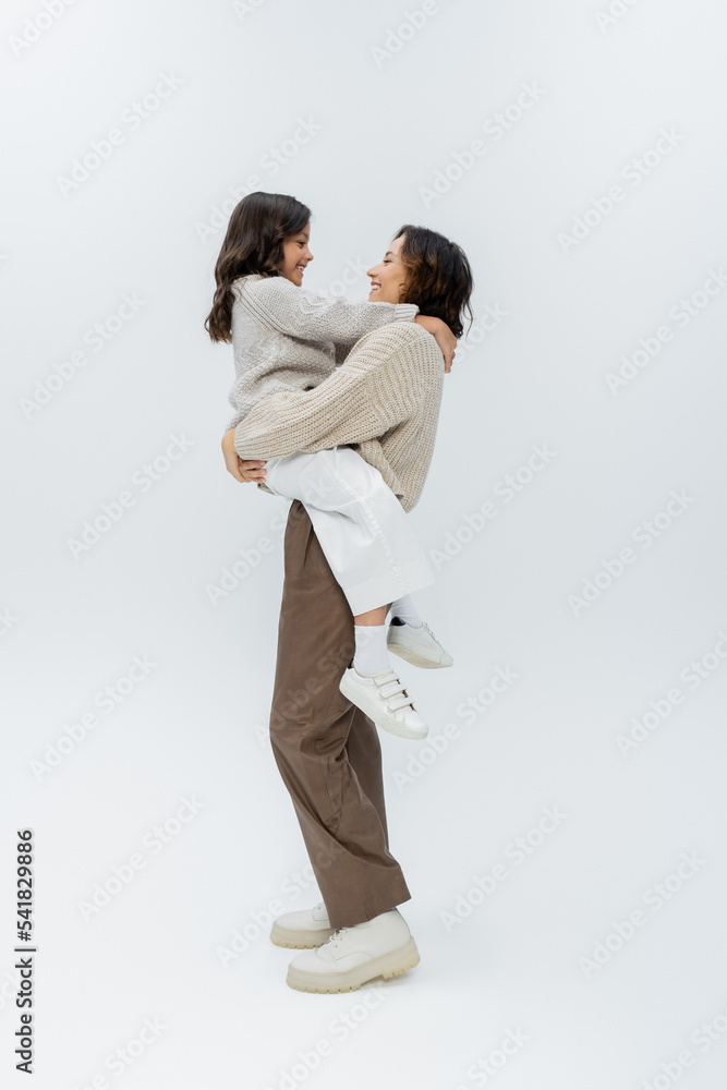 side view of woman in stylish autumn clothes holding daughter in hands on grey background side view of woman in stylish autumn clothes holding daughter in hands on grey background
