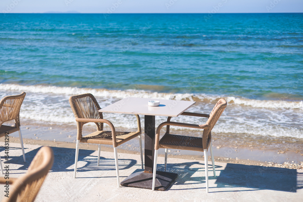 Restaurant terrace by the sea, seaside view cafe on the beach, empty chairs and tables Ionian sea shore, Greece, blue sea with crystal clear water