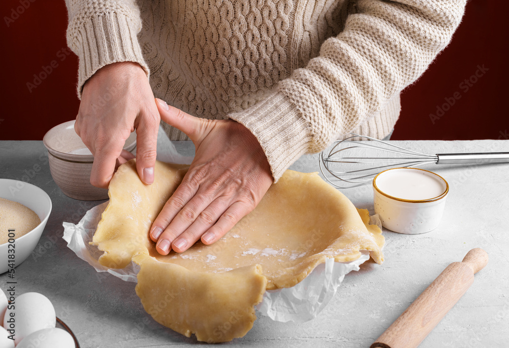 Woman arranging the dough in the pie pan on the table in the kitchen, female hands are putting