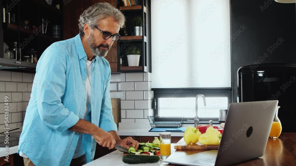 Senior man in kitchen watching laptop