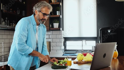 Senior man in kitchen watching laptop