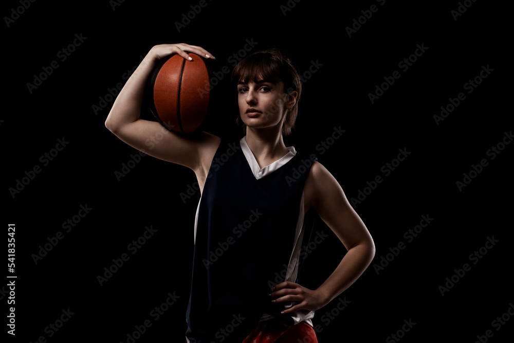 Female basketball player. Beautiful girl holding ball. Side lit half silhouette studio portrait against black background. Female basketball player. Beautiful girl holding ball. Side lit half silhouette studio portrait against black background.