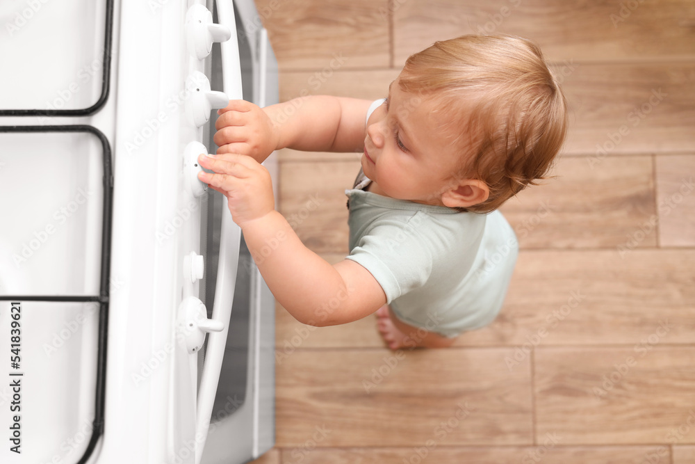 Little child playing with gas stove indoors, above view. Dangers in kitchen Little child playing with gas stove indoors, above view. Dangers in kitchen