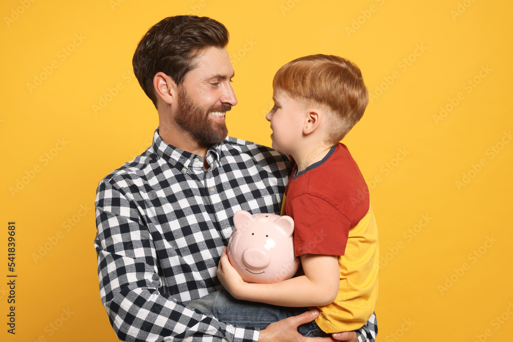 Father and his son with ceramic piggy bank on orange background Stock ...