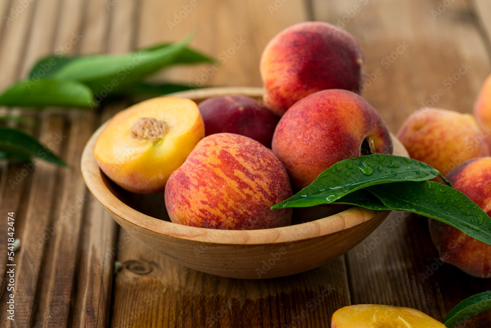Peaches with leaves in a wooden bowl with peach in halves on top. Flat lay composition with ripe juicy peaches. Harvest of peaches for food or juice. Top view fresh organic fruit, vegan food. Peaches with leaves in a wooden bowl with peach in halves on top. Flat lay composition with ripe juicy peaches. Harvest of peaches for food or juice. Top view fresh organic fruit, vegan food.