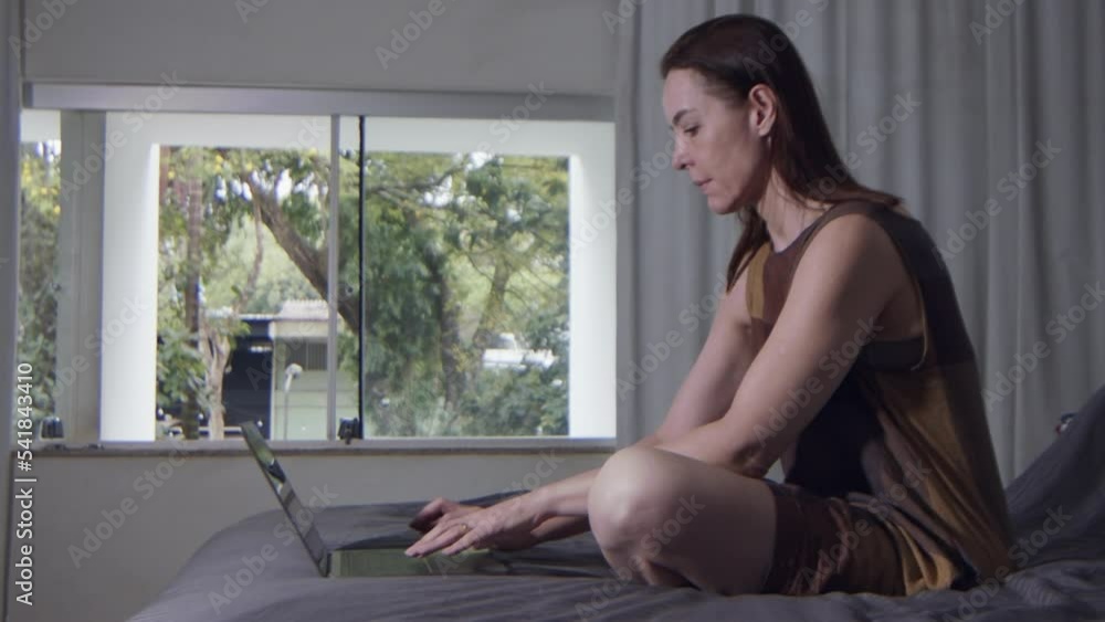 a female model is sitting on bed and working on her laptop computer, slow motion close up a female model is sitting on bed and working on her laptop computer, slow motion close up