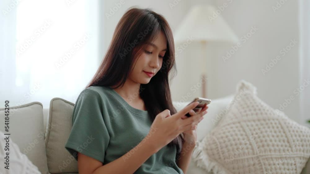 Happy young asian woman relax on comfortable couch at home texting messaging on smartphone, smiling girl use cellphone chatting, browse wireless internet on gadget, shopping online from home Happy young asian woman relax on comfortable couch at home texting messaging on smartphone, smiling girl use cellphone chatting, browse wireless internet on gadget, shopping online from home
